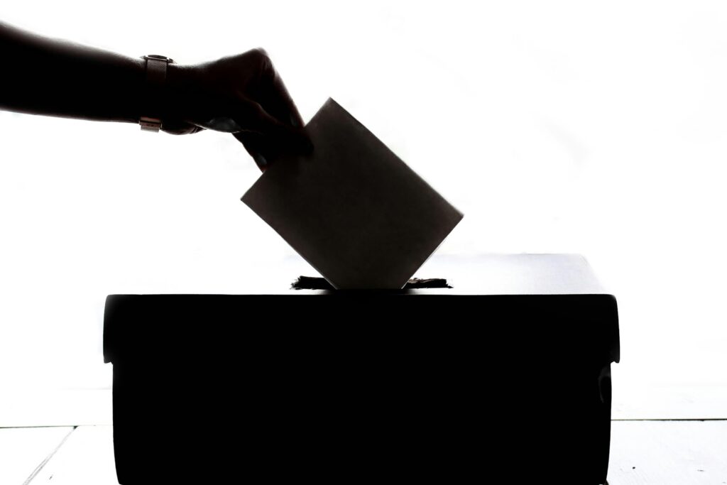 pexels-photo-1550337-1550337 Silhouette of a hand placing a vote into a ballot box, symbolizing democracy.